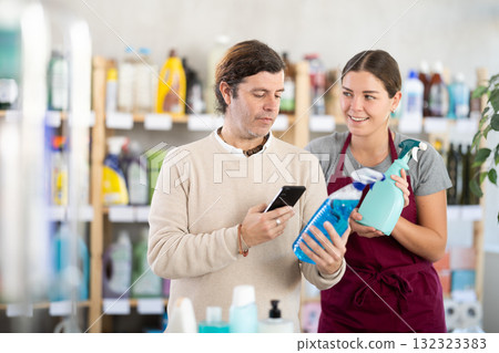 Man scanning bottle of cleaning spray with smartphone in store Man scanning bottle of cleaning spray with smartphone in store 132323383