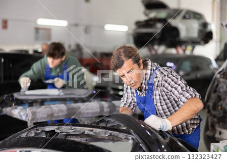 Experienced mechanic inspecting detached car bumper in workshop 132323427
