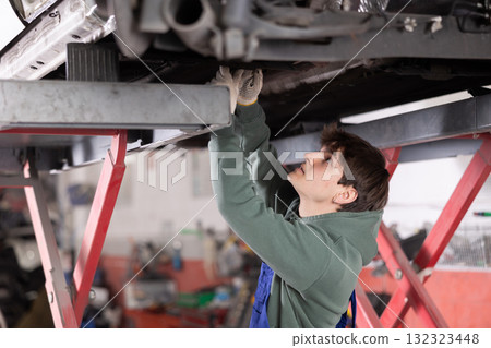 Young mechanic is repairing car - changing the shock absorber of the car rear suspension 132323448