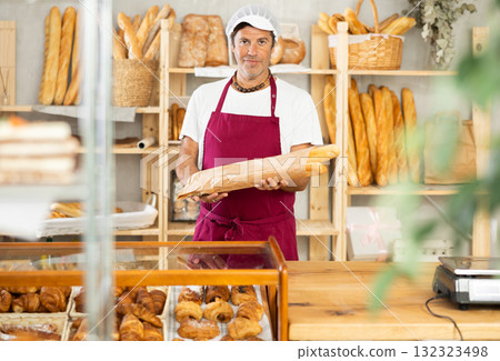 Middle-aged salesman holding paper bag with baguettes in bakery 132323498