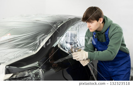 Focused young guy painting car with spray gun in workshop Focused young guy painting car with spray gun in workshop 132323518