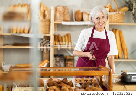 Mature saleswoman holding a service clip in bakery Mature saleswoman holding a service clip in bakery 132323522