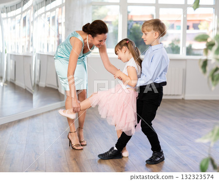 Cheerful ballet teacher correcting dance pose of preteen dancers 132323574