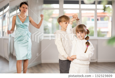 Couple of preteen dancers rehearsing ballroom dance while female teacher Couple of preteen dancers rehearsing ballroom dance while female teacher 132323609