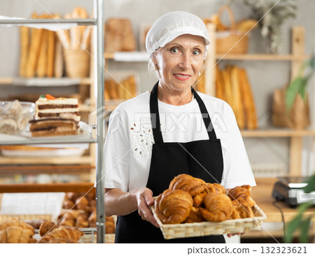Mature saleswoman displaying croissants in square wicker basket 132323621