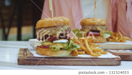large appetizing burger with meat and vegetables stands on the table next to a garnish of french fries overeating concept. Weight control, overeating calorie counting, junk food addiction 132324053