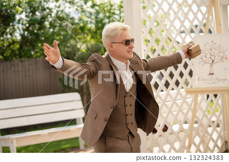 Man in stylish suit celebrating joyfully at a sunny outdoor event 132324383