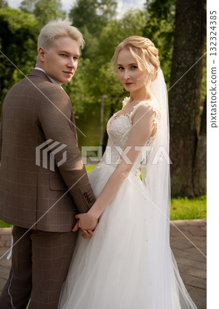 Young couple in elegant wedding attire holding hands outdoors 132324385