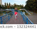 Young Woman Jogging Over a Scenic Bridge in a Beautiful Urban Park Setting 132324441