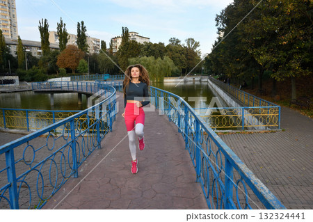 Young Woman Jogging Over a Scenic Bridge in a Beautiful Urban Park Setting 132324441