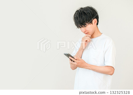 A young Asian man thinking, considering, worrying while looking at his smartphone A young Asian man thinking, considering, worrying while looking at his smartphone 132325328