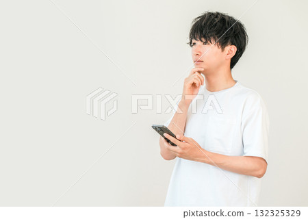 A young Asian man thinking, considering, worrying while looking at his smartphone A young Asian man thinking, considering, worrying while looking at his smartphone 132325329