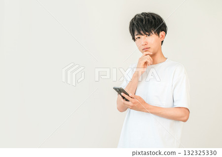 A young Asian man thinking, considering, worrying while looking at his smartphone A young Asian man thinking, considering, worrying while looking at his smartphone 132325330