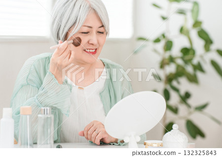 A senior Asian woman with gray hair applying makeup with a cheek brush and face brush 132325843