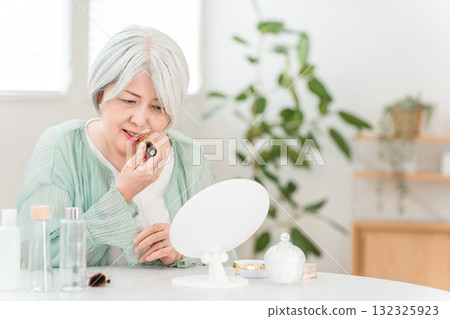A senior Asian woman with gray hair applying makeup (lipstick, rouge, gloss, lip) A senior Asian woman with gray hair applying makeup (lipstick, rouge, gloss, lip) 132325923