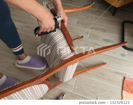 Anonymous person restore old vintage chair in home. Fabric replacement. Antique furniture and modern striped linen and cotton fabric. Hobbies, crafts, and retro-minimalist style. Anonymous person restore old vintage chair in home. Fabric replacement. Antique furniture and modern striped linen and cotton fabric. Hobbies, crafts, and retro-minimalist style. 132326121