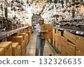 Smiling woman carries boxes in a well-lit home improvement store aisle filled with lighting fixtures 132326635