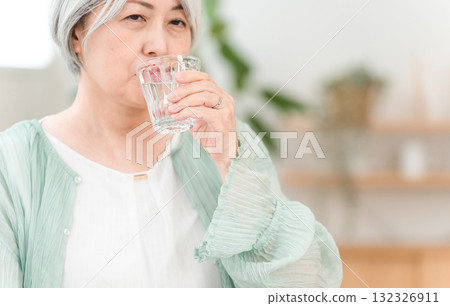 A gray-haired senior woman drinking mineral water in the living room at home 132326911