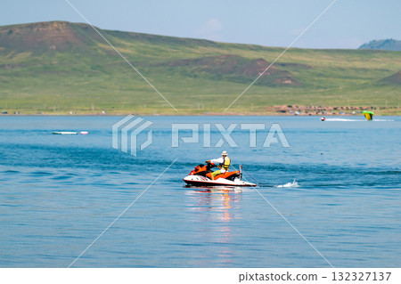 A man in a life jacket floats on a scooter on a lake. 132327137