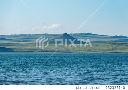 A mountain in the middle of a plain on the shore of a lake. A mountain in the middle of a plain on the shore of a lake. 132327140