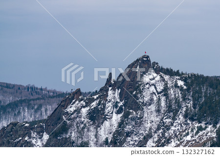 A majestic rock with a red flag on the mountaintop. A majestic rock with a red flag on the mountaintop. 132327162