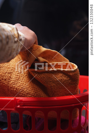 Hand putting towels into a red laundry basket 132330848