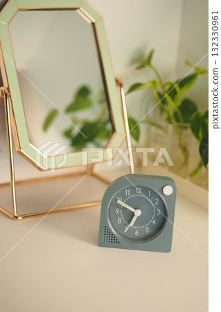 Modern clock displayed on a desk near a plant and mirror Modern clock displayed on a desk near a plant and mirror 132330961
