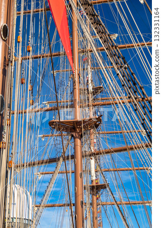 Vintage tall ship with red sail and intricate rigging against blue sky 132331164