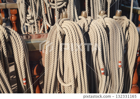 Coiled ropes aligned on belaying pins of a sailing ship indicating active sea voyages. Neat organization ensures efficient sail adjustments or anchoring. Coiled ropes aligned on belaying pins of a sailing ship indicating active sea voyages. Neat organization ensures efficient sail adjustments or anchoring. 132331165
