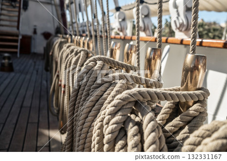 Neatly coiled ropes on the deck of a traditional sailing ship, resting on polished metallic pins. Classic maritime scene depicting organized sail rigging Neatly coiled ropes on the deck of a traditional sailing ship, resting on polished metallic pins. Classic maritime scene depicting organized sail rigging 132331167