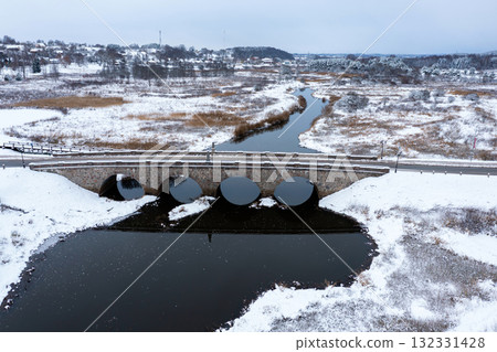 An old stone bridge with arches over the Abava river on a snowy winter day, Kandava, Latvia An old stone bridge with arches over the Abava river on a snowy winter day, Kandava, Latvia 132331428