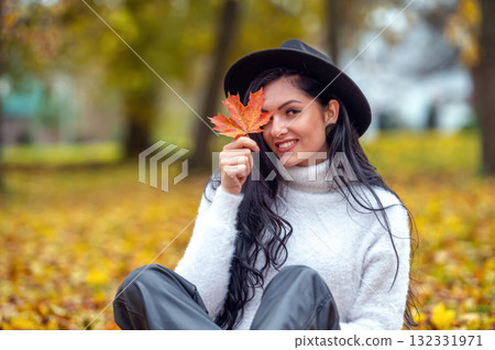 Portrait of a beautiful young woman in the autumn park with maple leaf 132331971