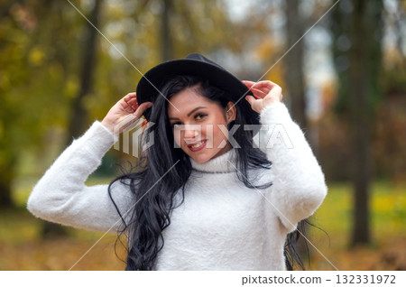 Young beautiful brunette woman in a white sweater and black hat in an autumn park 132331972