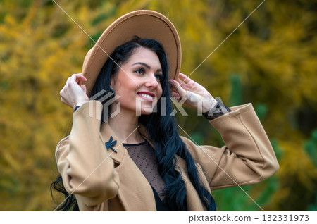 Beautiful brunette girl in beige coat and hat posing in autumn park 132331973