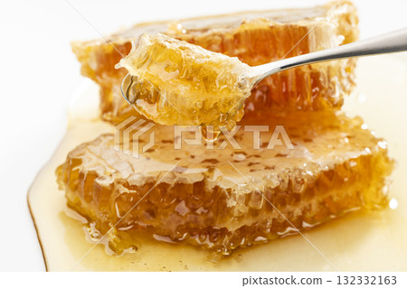 Honey dripping from a honeycomb scooped up with a spoon Honey dripping from a honeycomb scooped up with a spoon 132332163