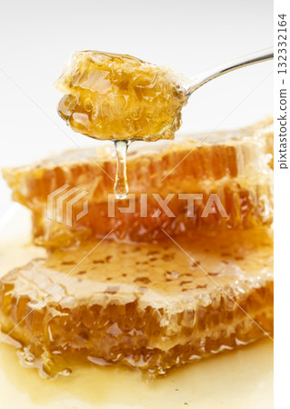 Honey dripping from a honeycomb scooped up with a spoon 132332164