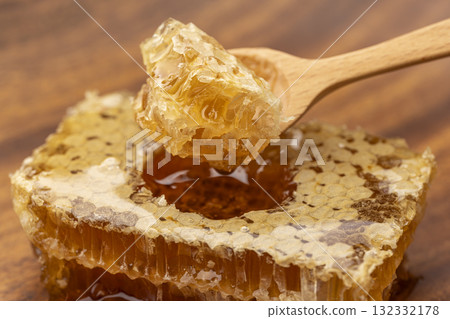 蜂巢蜜的特寫,展示了用木勺舀起的蜂蜜的美麗光澤和質地 蜂巢蜜的特寫,展示了用木勺舀起的蜂蜜的美麗光澤和質地 132332178