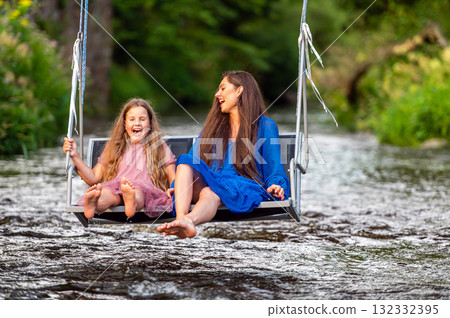 a woman and a young girl are swinging across a fast-flowing river, laughing and splashing with water a woman and a young girl are swinging across a fast-flowing river, laughing and splashing with water 132332395