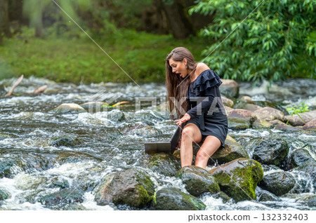 female freelancer sitting on a rock in the river and dropping her laptop into the water female freelancer sitting on a rock in the river and dropping her laptop into the water 132332403