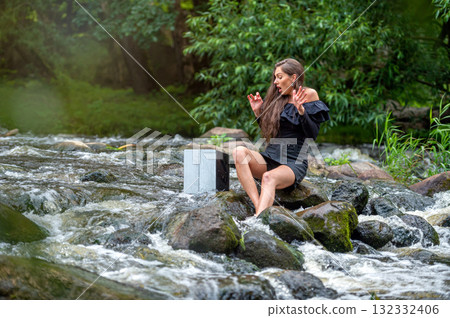 female freelancer sitting on a rock in the river and dropping her laptop into the water 132332406
