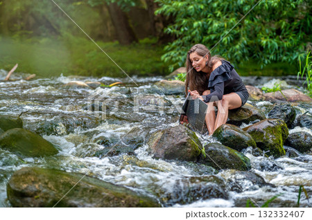 worried woman pulls out of water laptop that fell into river, remote holiday work accident 132332407