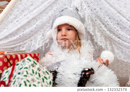 portrait of a cute little girl child wearing a silver color Christmas hat sitting between gift boxes portrait of a cute little girl child wearing a silver color Christmas hat sitting between gift boxes 132332578