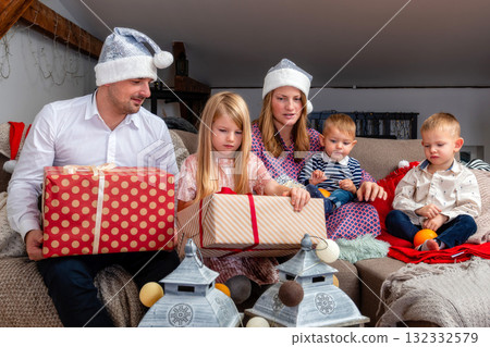 happy family sitting on the sofa in the living room and unpacking Christmas presents, the concept of a family holiday happy family sitting on the sofa in the living room and unpacking Christmas presents, the concept of a family holiday 132332579