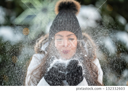 young woman blows snow from her hands while standing against the background of a Christmas tree young woman blows snow from her hands while standing against the background of a Christmas tree 132332603