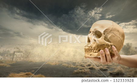 Human hand holding human head skull with dark and dramatic cloudscape background. The scene is scary and mysterious. Concept of Spooky Halloween Human hand holding human head skull with dark and dramatic cloudscape background. The scene is scary and mysterious. Concept of Spooky Halloween 132333928
