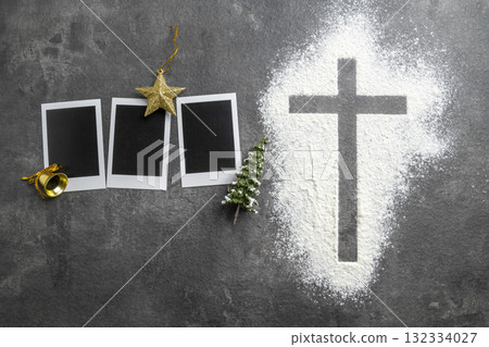 Christian cross formed by a dusting of white powder with instant camera photo frame and miniature Christmas trees, golden star and bell. Concept of faith, holiday celebration, and spiritual reflection 132334027