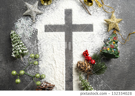 Christian cross formed by a dusting of white powder with various colorful Christmas ornaments on the table. Concept of faith, holiday celebration, and spiritual reflection 132334028