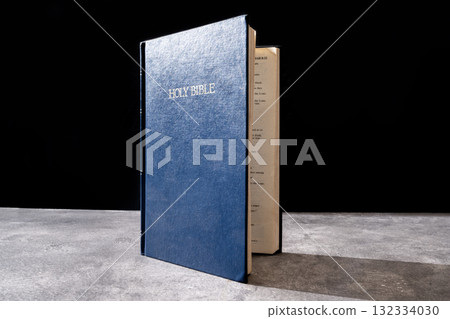 Blue book of the Holy bible. Standing on the table with a dark background. Symbol of faith in God. Concept of Spirituality, Christianity, religion, faith, Jesus, or belief 132334030