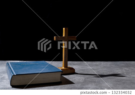 Blue book of the Holy bible and Christian cross. Standing on the table with a dark background. Symbol of faith in God. Concept of Spirituality, Christianity, religion, faith, Jesus, or belief 132334032
