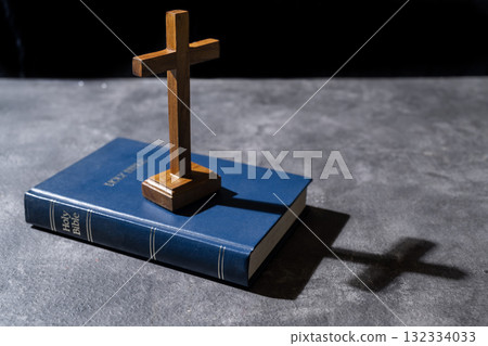 Blue book of the Holy bible and Christian cross. Standing on the table with a dark background. Symbol of faith in God. Concept of Spirituality, Christianity, religion, faith, Jesus, or belief 132334033